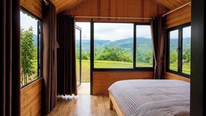 Een slaapkamer met een houten plafond, grote ramen, een bed en gordijnen.
