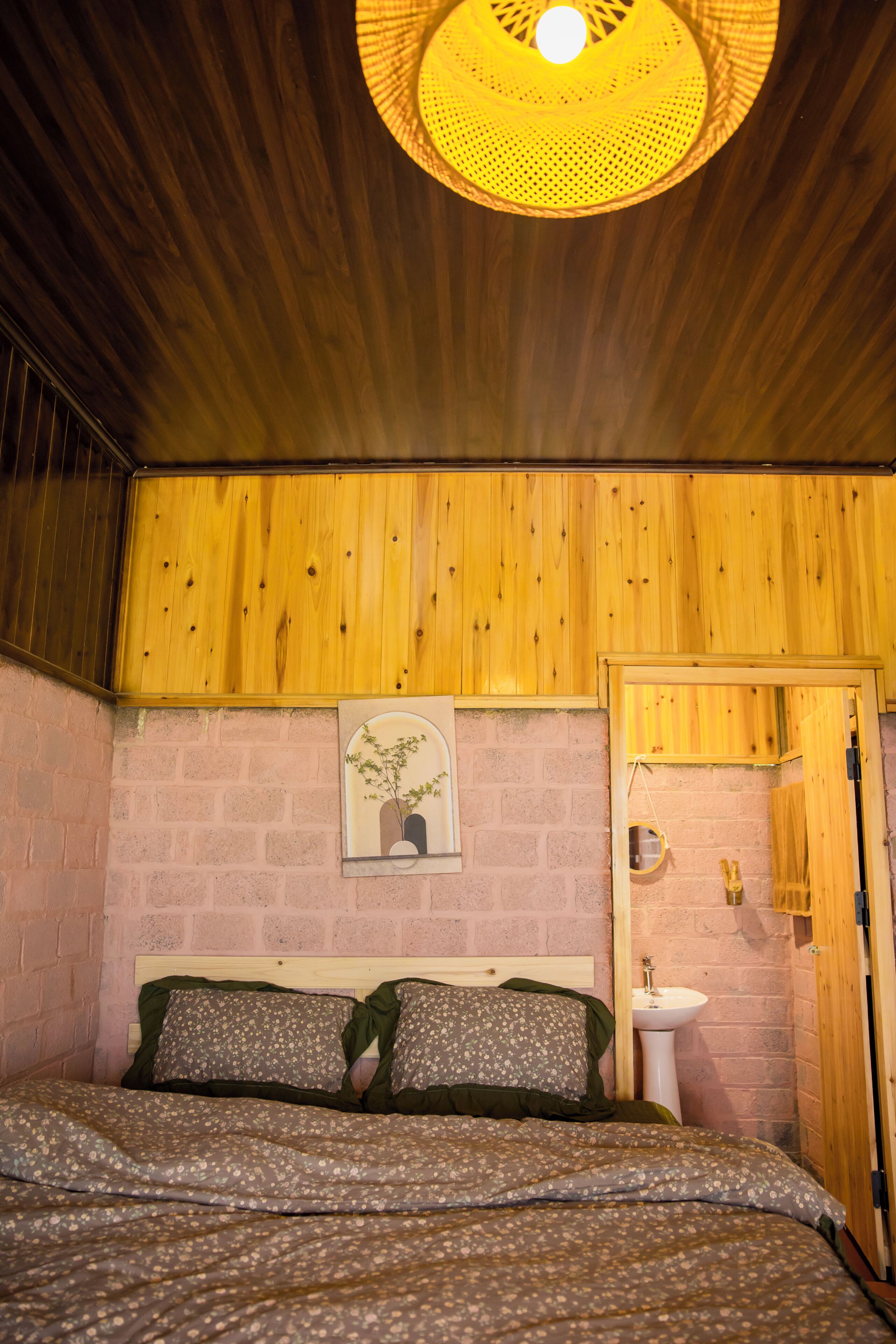 Ein Schlafzimmer mit Holzboden, einem Bett mit Blumenmuster-Bettwäsche, einem Wandbild, einem Nachttisch und einer Holztür.