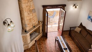 Uma sala de estar aconchegante com lareira de pedra, um banco de madeira, um sofá e vista para o pátio externo.