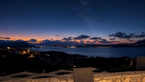 Sternenklarer Nachthimmel, Blick auf das Meer und eine ferne Stadtansicht.
