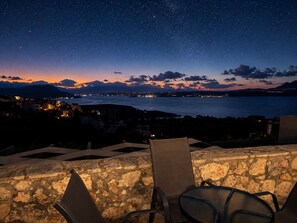 Sternenklarer Nachthimmel, Blick auf das Meer und eine ferne Stadtansicht.