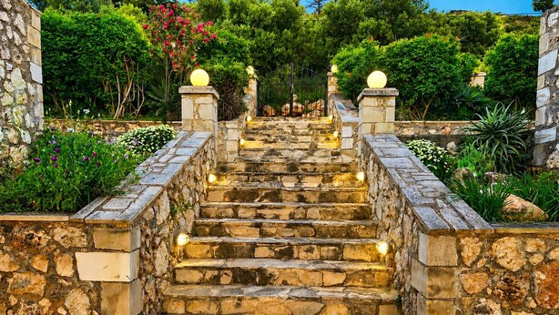 Eine Steintreppe mit Stufen, umgeben von Grünflächen und Steinmauern.