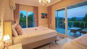 A bedroom with a large bed, a chandelier, a view of the outdoors, and a balcony with furniture. - Premium 4 bedroom villa in Oludeniz (Fethiye)