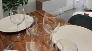 A dining area with a wooden table, clear glassware, a potted plant, and a mounted flat-screen TV.