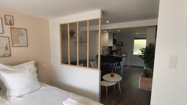 A bedroom with a bed, a bedside table, a mirror, and a view into the kitchen area.