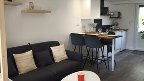 A modern living space with a black sofa, two white tables, a kitchen area with a dining table, and built-in cabinets.