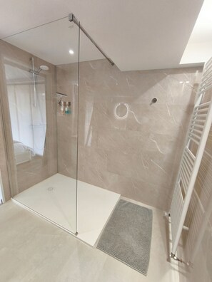 Un espace douche moderne doté d’une porte en verre, d’un pommeau de douche blanc et d’un panneau de commande.