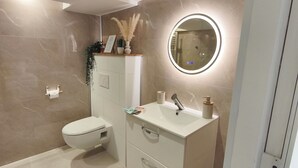 A modern bathroom with a toilet, vanity, and a round mirror with lighting.