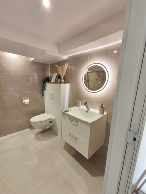 Un baño moderno con inodoro, tocador y un espejo redondo con iluminación.