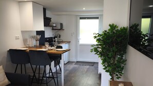 A modern kitchen with white cabinets, a dining area with a round table and chairs, a small potted plant, and a large window.