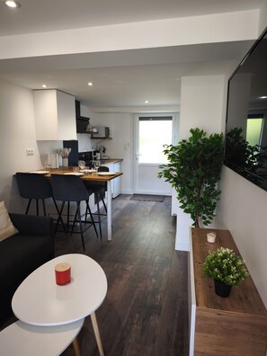 Une cuisine moderne avec des meubles blancs, un coin repas comprenant une table ronde et des chaises, une petite plante en pot et un grand miroir.