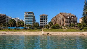 Un hotel frente a la playa con varios edificios altos, agua azul cristalina y palmeras.