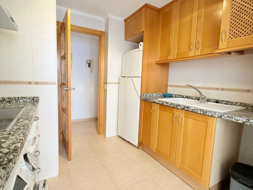Una cocina con armarios de madera, encimera de granito, horno empotrado y refrigerador.