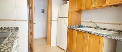 Una cocina con armarios de madera, encimera de granito, horno empotrado y refrigerador.