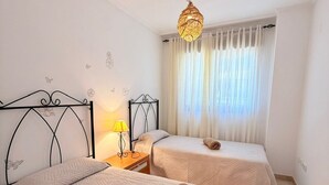 Habitación de hotel con dos camas, una mesita de noche, una lámpara y un ventanal con cortinas.