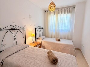 Ein Hotelzimmer mit zwei Betten, einem Nachttisch, einer Lampe und einem Fenster mit Vorhängen.