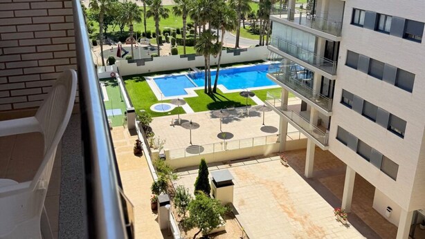 Vista de una piscina, palmeras y una playa desde un balcón.