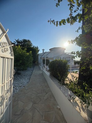 A pathway leading to a building with a circular structure, surrounded by greenery and a white fence.