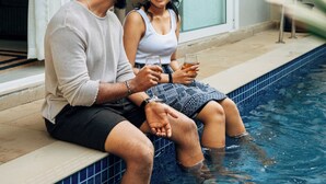 Um casal sentado perto de uma piscina, com porta de vidro e chão de azulejos.