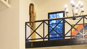 Interior espaçoso com teto alto, escada e vista para o exterior pela janela.