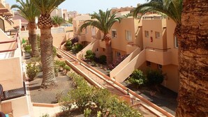 A residential area with multiple buildings, palm trees, and a central walkway. - Lovely   Apt  Siesta (Corralejo)