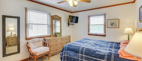 A bedroom with a bed, a dresser, a chair, a ceiling fan, and a television.
