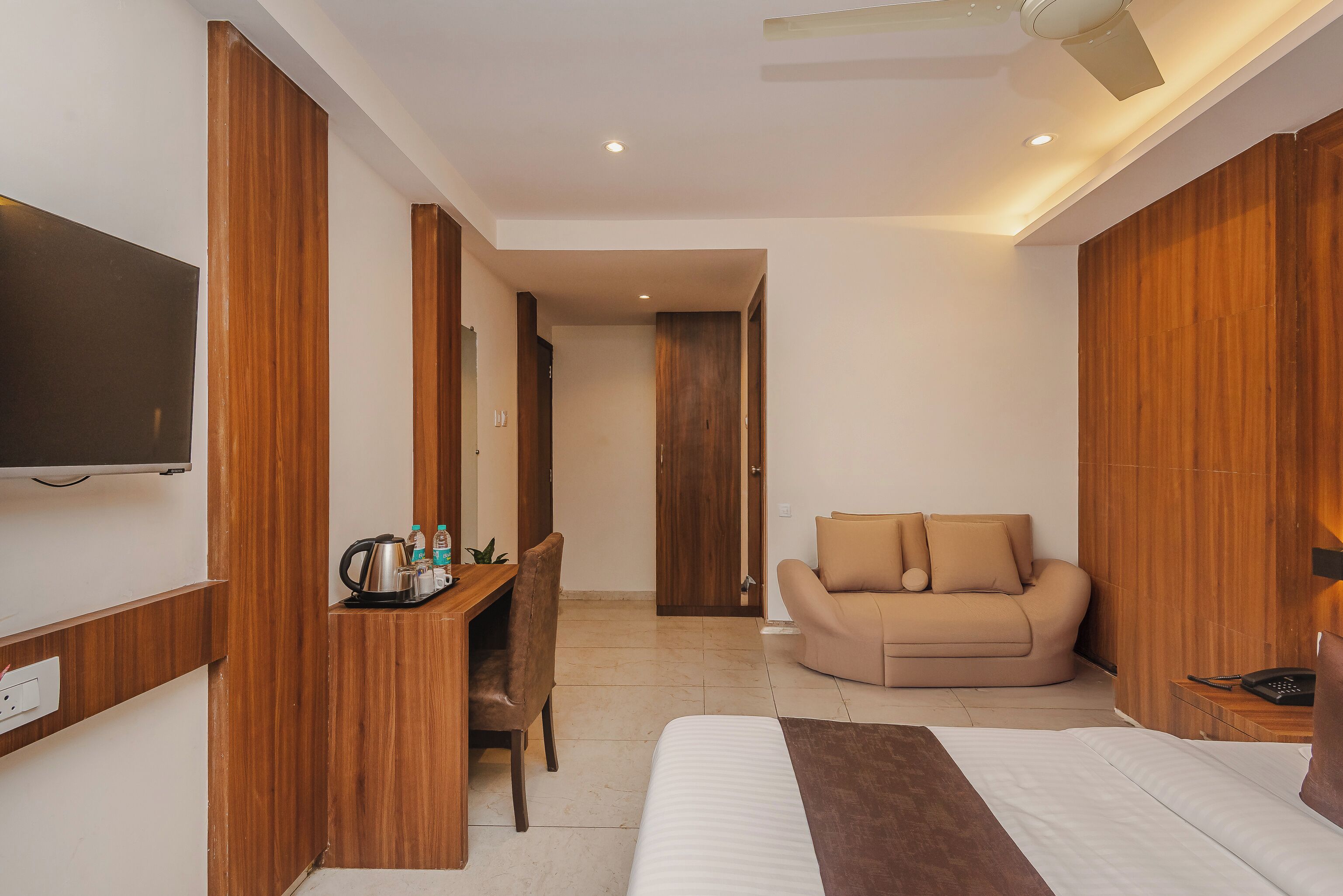 A hotel room with a bed, a sofa, a desk with a kettle, and a television.