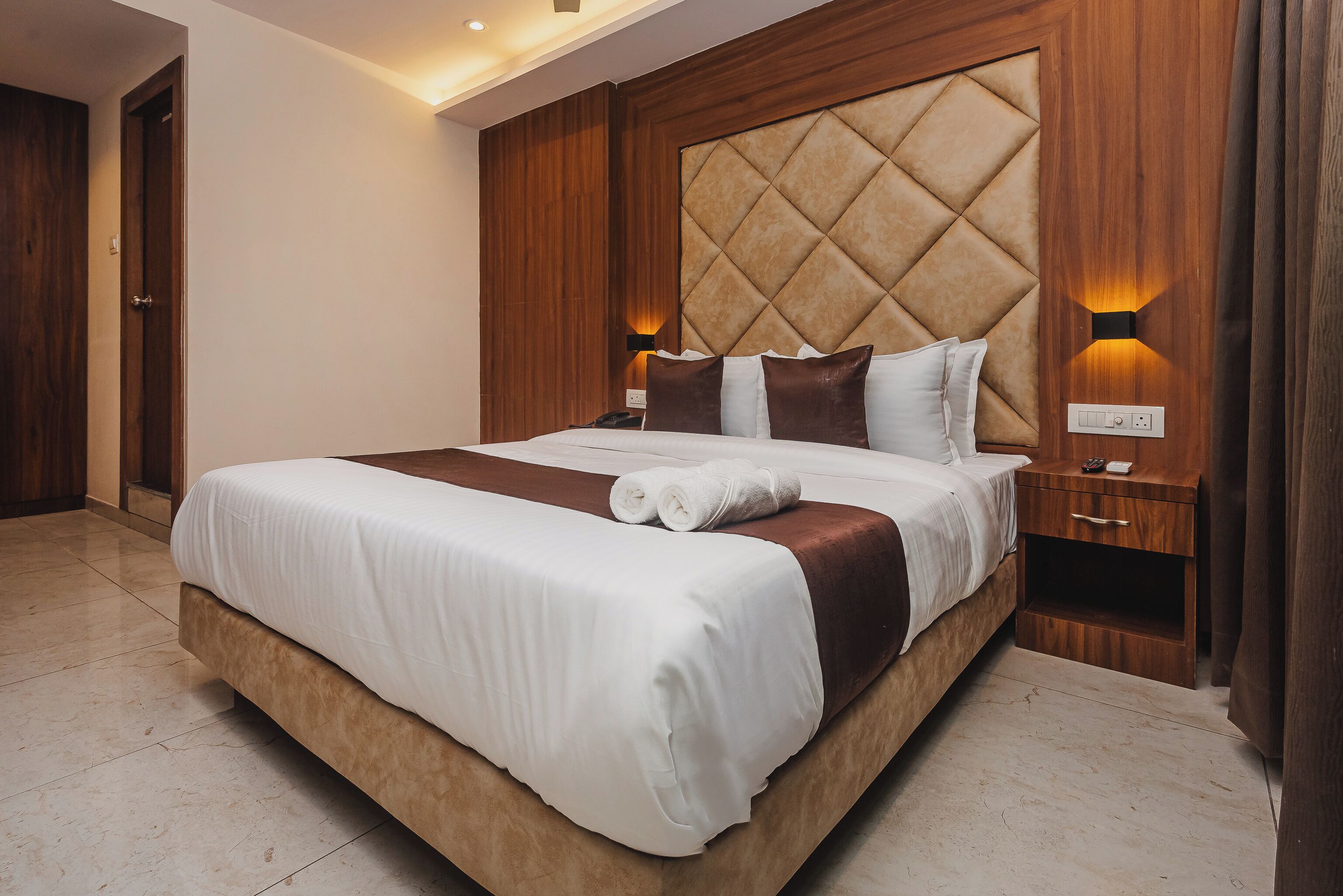 A hotel room with a large bed, wooden headboard, bedside lamps, and a nightstand.