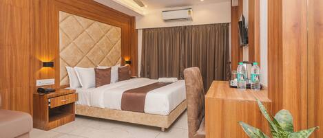 A modern hotel room with a bed, bedside table, chair, desk, and a potted plant.