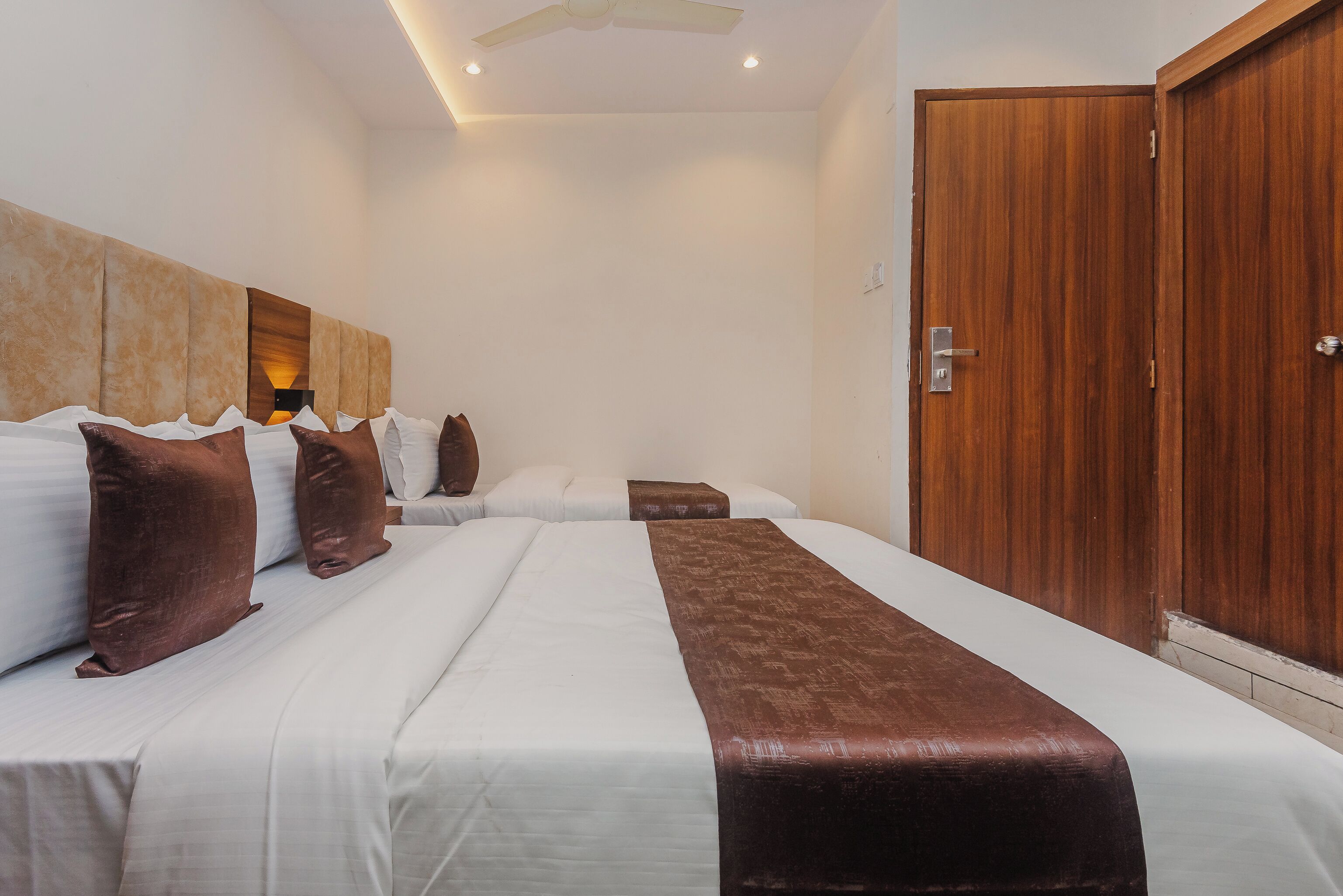 A hotel room with two beds, a wooden wardrobe, and a ceiling fan.