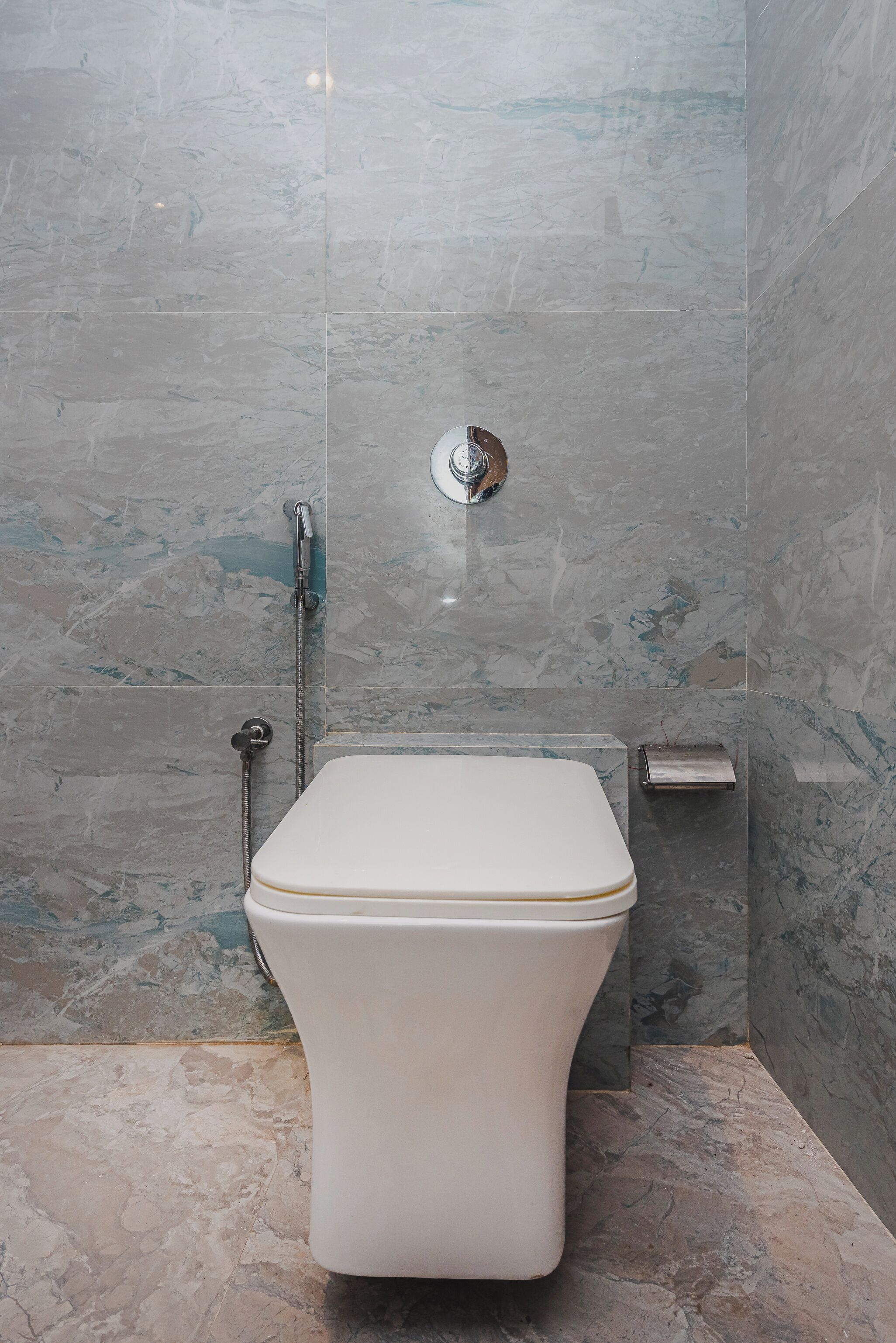 Een moderne badkamer met een wit toilet, een douchecabine en een marmeren wand.