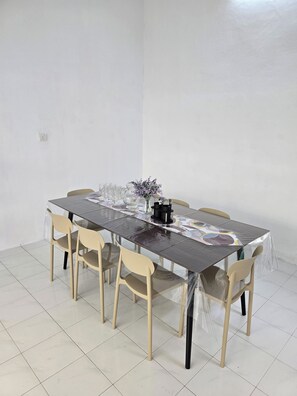 A dining table with chairs, a vase with flowers, and a black object on the table.
