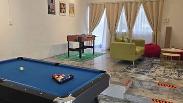 A pool table with balls, a sofa, a green armchair, a red chair, and a small table with a plant.