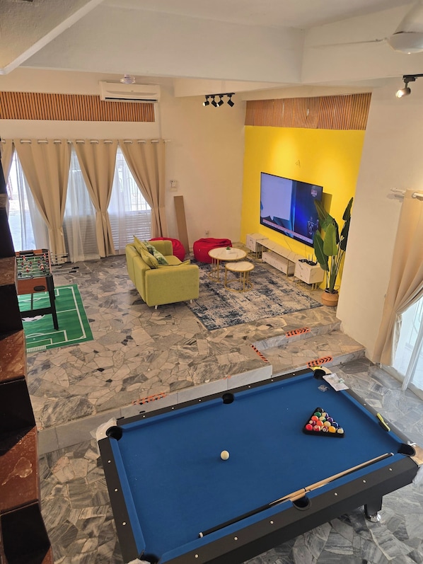 A pool table, a sofa, a television, and a window with curtains.