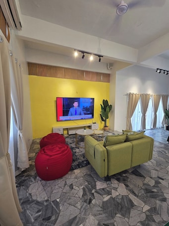 A living room with a television, a sofa, a red bean bag, a cactus, and a patterned floor.. SD Homestay 81 Play together, Fun forever