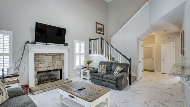 Una sala de estar con chimenea, televisor, sofá, mesa de centro y escalera.