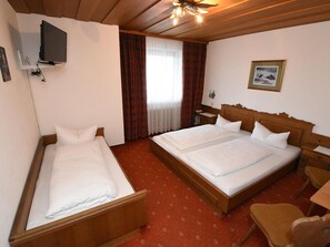Een hotelkamer met twee bedden, een televisie, een houten plafondventilator, een ingelijst schilderij aan de muur en een rode vloerbedekking.