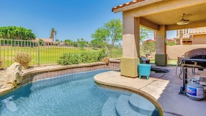 A swimming pool with a patio area, a barbecue grill, and a view of a golf course.