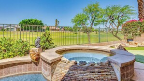A hot tub with a brick fire pit, surrounded by a fence, with a view of a golf course and trees.