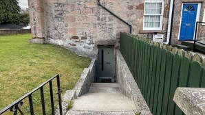 A stone building with a narrow entrance, a blue door, and a green fence. - Heather & Stone Bothy, Inverness (Inverness)