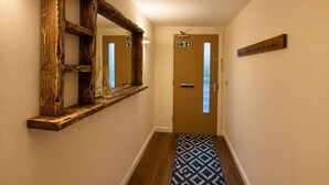A hallway with a wooden-framed mirror, a fire exit sign, a door, and a wall-mounted coat rack. - Heather & Stone Bothy, Inverness (Inverness)