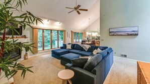 Ein geräumiges Wohnzimmer mit Ecksofa, Deckenventilator, großen Fenstern und Essbereich.