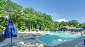 Ein Schwimmbad mit Liegestühlen und Sonnenschirmen, umgeben von Bäumen.