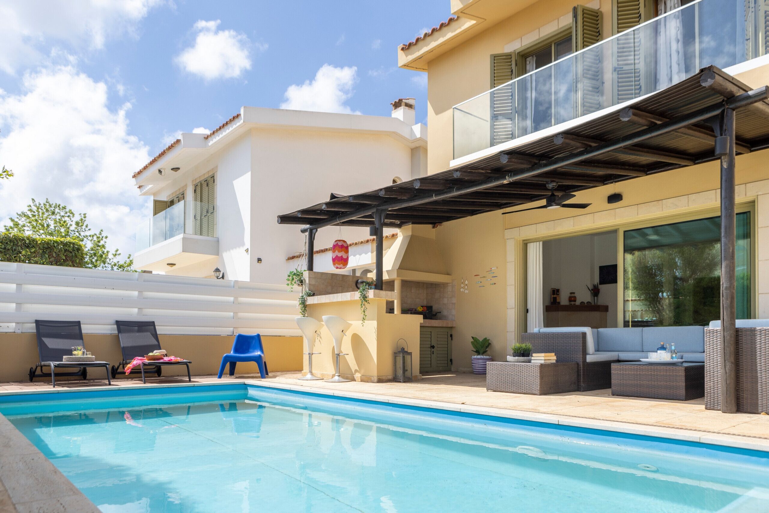 A poolside area with lounge chairs, a covered patio, and a large window overlooking the pool.