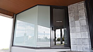 Un bâtiment moderne doté d’une grande fenêtre en verre, d’une porte en métal portant l’inscription « STUDIO TWO » et d’un mur en pierre à la texture particulière.
