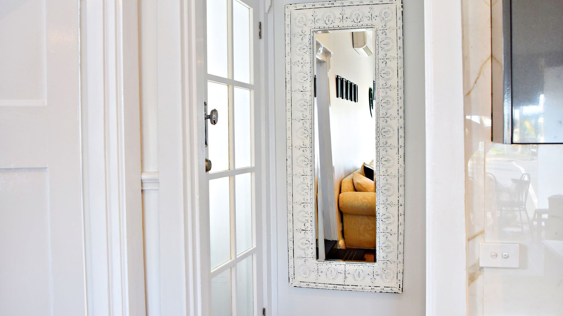 Une porte blanche avec un miroir qui reflète une pièce contenant une chaise et une table.