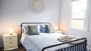 Une chambre à coucher avec un lit, des tables de chevet, un miroir mural et une fenêtre.