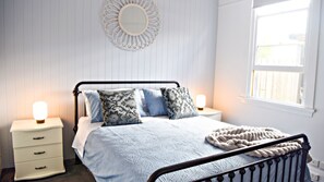 Ein Schlafzimmer mit einem Bett, Nachttischen, einem Wandspiegel und einem Fenster.
