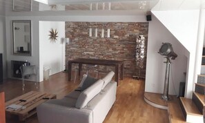 Una sala de estar con pared de piedra, un sofá, una mesa de centro y una escalera.