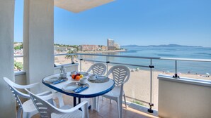 A balcony with a table set for two, overlooking a beach and ocean. - RIELLS: Fully renovated seafront apartment (L'Escala)